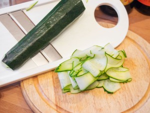 Die Zucchini wird von der längsseite mit einem Gemüsehobel in feine Scheiben geschnitten.