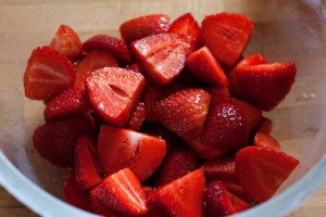 Halbierte und geviertelte Erdbeeren werden mit Zucker bestreut.