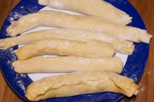 Nachdem Semmelbrösel auf den butterbestrichenen Teig gestreut wurden, werden die Klöße gewickelt. Die aufgerollten Wickelklöße werden auf einem Teller beiseite gestellt.